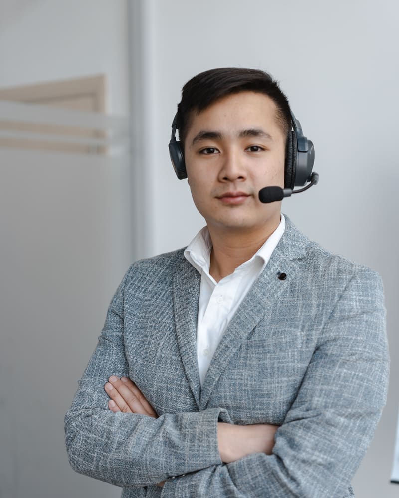 Boulevard customer support representative in a grey blazer wearing a headset, standing with arms folded in a bright office